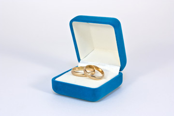 Two gold wedding rings in an open heart blue box