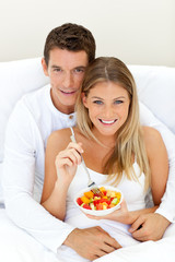 Obraz na płótnie Canvas Loving couple eating fruit lying on their bed