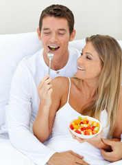 Obraz na płótnie Canvas Jolly couple eating fruit lying on their bed