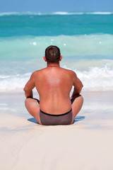 Tanned man meditate on the beach