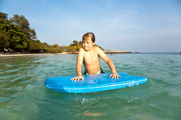 boy is swimming on his surfboard and happily smiling