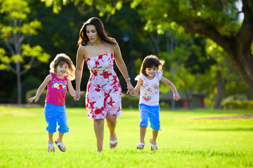 Fototapeta premium Excited mum and two daughters jumping in grass