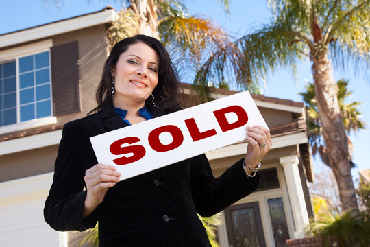 Attractive Hispanic Woman Holding Sold Sign In Front of House