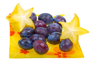 Carambola and plums on a plate isolated on white