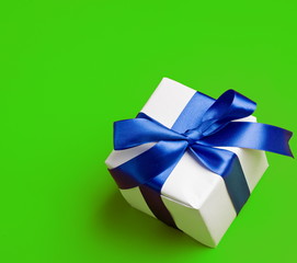 white gift in a blue  ribbon on a green background