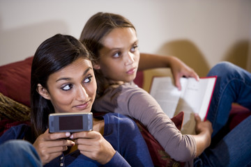 Girls reclining on sofa look up from texting and reading book