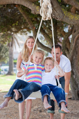 Joyful parents pushing their children on a swing