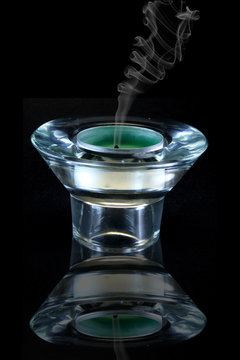 green candle in glass holder with smoke and reflection