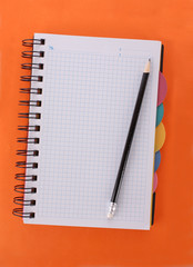 Notebook with pencil on the orange background