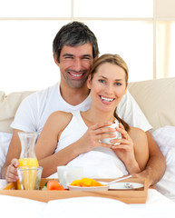 Obraz na płótnie Canvas Smiling couple having breakfast lying in the bed