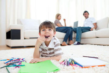 Pensive little boy drawing lying on the floor