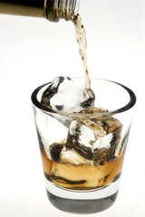 Whiskey being poured over ice cubes on a white background