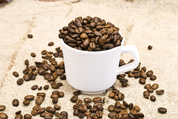 Coffee beans with white cup on sackcloth