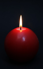 Red round shining candle on a black background