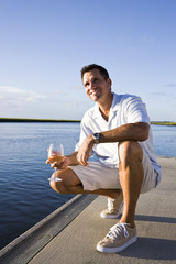 Fototapeta na wymiar Mid-adult man on dock by water enjoying drink on sunny day
