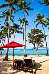 Red umbrella and chairs on sand beach in tropic