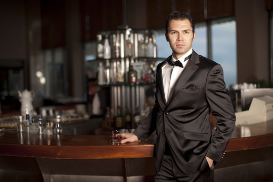 Handsome man in tuxedo at bar holding whisky in hand