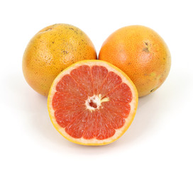 A single cut grapefruit with two uncut fruits