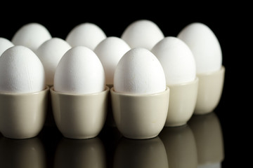 white chicken eggs in egg-cups on black reflecting background