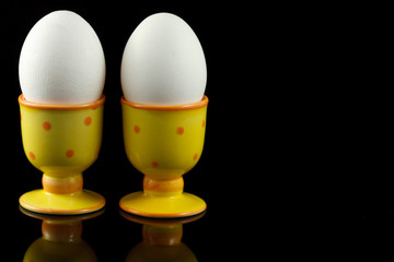 chicken eggs in dotted eggcups on reflecting black background