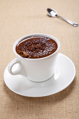 hot chocolate in white mug, saucer and spoon, on jute backdrop