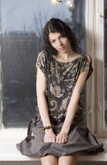 Sad young woman sitting on the windowsill