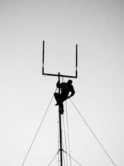 silhouette of worker hanging from antenna and reaching for tool