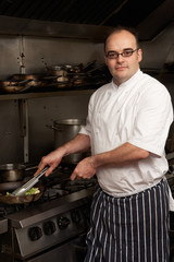 Male Chef Preparing Meal On Cooker In Restaurant Kitchen