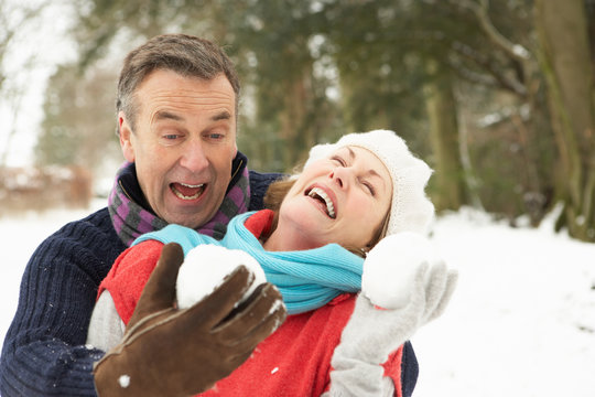 Senior Couple Having Snowball Fight In Snowy Woodland