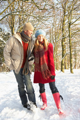 Fototapeta na wymiar Couple Walking Through Snowy Woodland