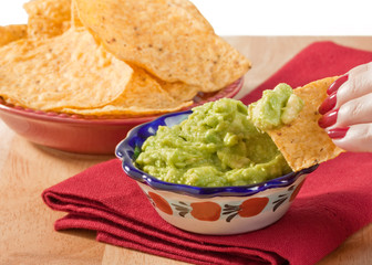 Woman's hand dipping tortilla chip into guacamole