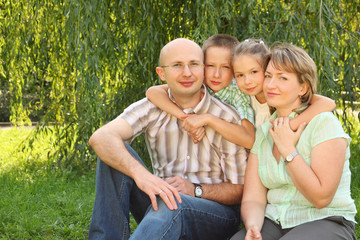 family with two children sitting at the grass near osier