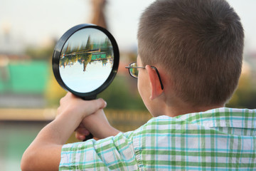 little boy is looking through magnifier in early fall park
