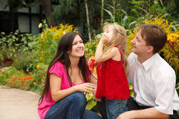 Parents observe as their daughter blows soap bubbles in garden.
