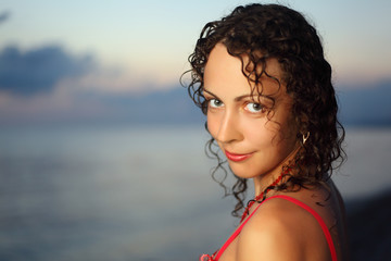 Curly beautiful young woman near sea in evening