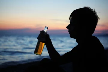 Fotobehang Bar Silhouette teenager boy with beer bottler on stone seacoast