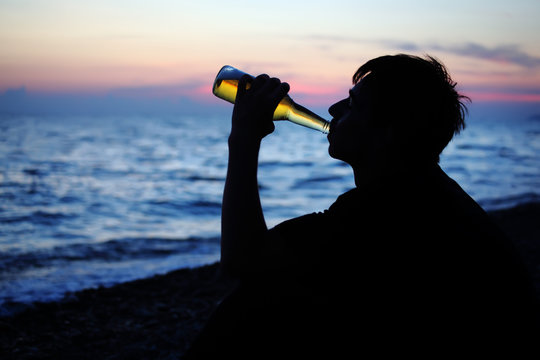 Silhouette Teenager Boy Drinking Beer On Stone Seacoast