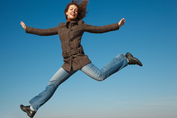 Fototapeta na wymiar Girl in coat and jeans in jump against blue sky