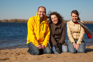 Three young men sit on bank of river sunny autumn day.