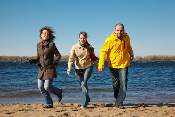 Three young men running down beach at camera holding hands