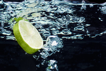 Fototapeta na wymiar Slice of lime (lemon) falling in water near surface