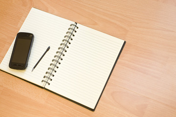 Mobile and Notebook on Wooden Table
