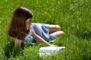 Fototapeta premium Girl reading book lying on green meadow