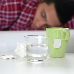Tee, Tabletten und Glas Wasser vor kranker Person