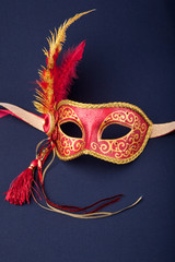 red and gold feathered mask on a dark background.
