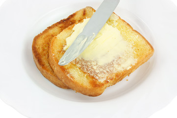 Knife spreading butter on toast in white plate