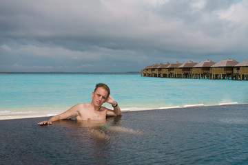 Sports man has a rest in pool with kind on ocean, Maldives