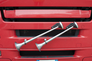 Detail of some air horns near a red truck’s radiator