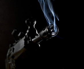 smoke rising from the barrel of an assault rifle on a dark background - obrazy, fototapety, plakaty