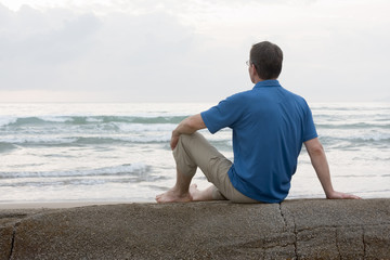Fototapeta na wymiar Mann sitzt auf Fels am Strand